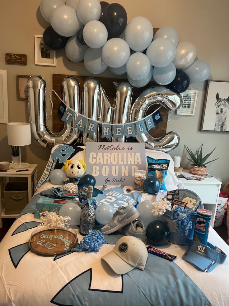 a bed topped with lots of blue and white balloons next to a giant silver balloon