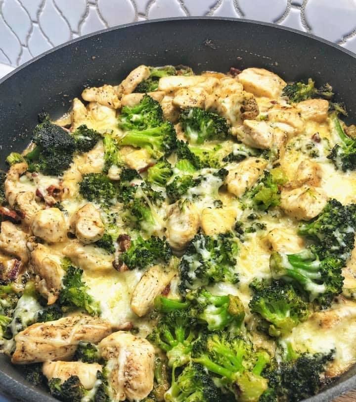 a skillet filled with chicken and broccoli covered in cheese