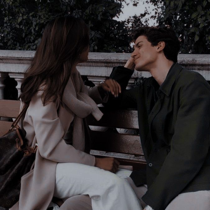 a man and woman sitting on a park bench talking to each other while holding hands