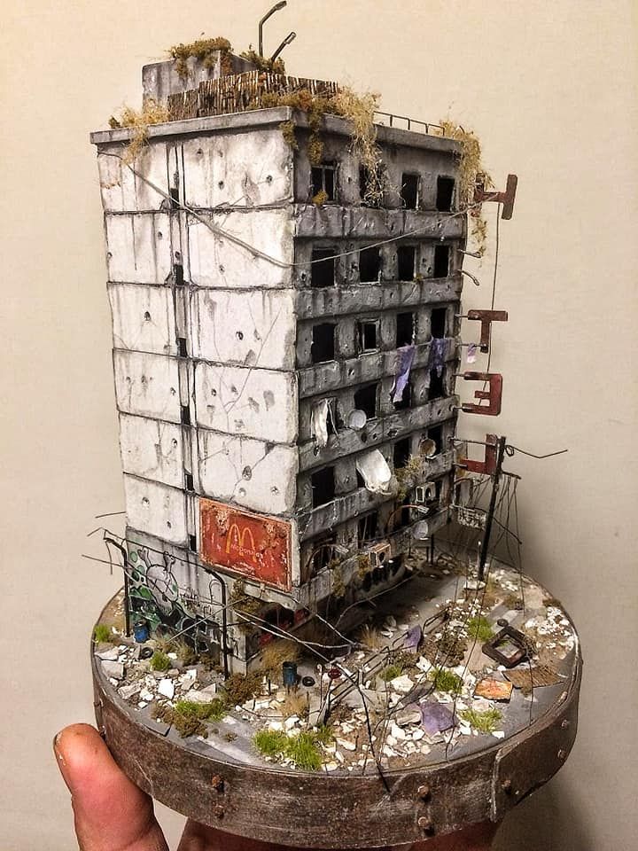 a person holding up a model of a building made out of junk and other items