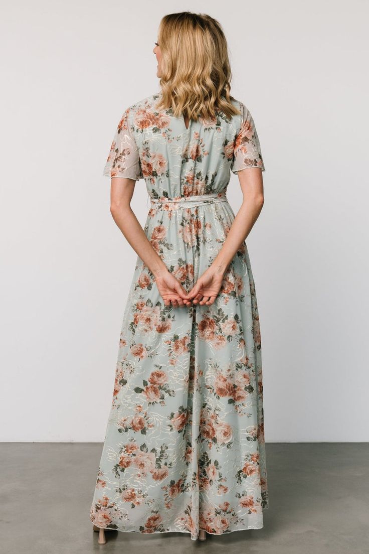 Introducing the Katalaya Maxi Dress, an easy, modest, and feminine choice for semi-formal occasions. Crafted in soft Sage Green with muted florals, it features a tulle overlay adorned with delicate Gold floral embroidery, a round neckline, elastic-back waist with a self-tie sash, and sheer flutter sleeves for an effortlessly elegant look. Spring Wedding Guest Maxi Dress With Short Sleeves, Floral Print Short Sleeve Dresses For Wedding Guests, Modest Maxi Dress For Garden Party, Modest Flowy Floral Dress For Garden Party, Modest Flowy Floral Dress For Casual Wear, Modest Flowy Floral Dress For Casual Occasions, Modest Fitted Floral Maxi Dress, Modest Fitted Dress With Floral Embroidery, Modest Floral Print Maxi Dress For Garden Party