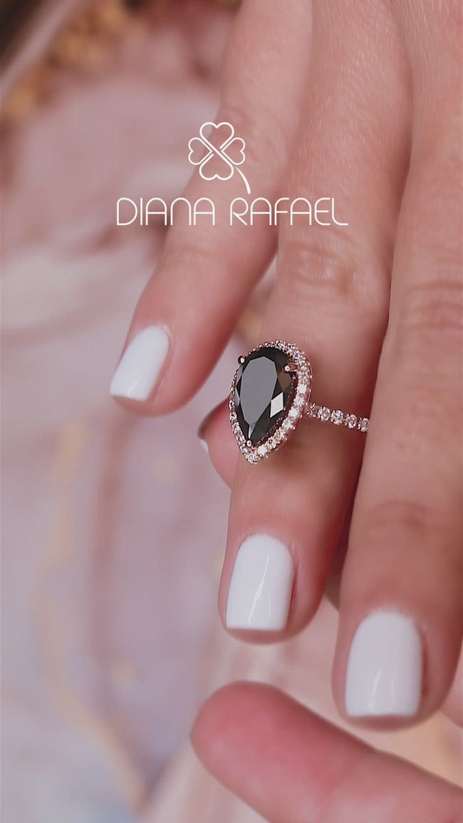 a woman's hand with white and black nail polish holding a diamond engagement ring