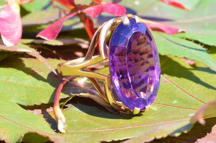 "The Brookside Outstanding Amethyst Cocktail Ring. The ring features an amazing, over 20 carat oval brilliant cut vivid purple amethyst in the center. Finished with a mid century modern filigree type shank in the through finger view the ring makes a statement. The ring is crafted in 18 karat yellow gold and is signed by the designer with the hallmark \"CB\" Yet we have not quite identified the craftsman quite yet. An amazing statement piece and a benchmark for the mid century modern era. Each pi Art Deco Oval Purple Amethyst Ring, Art Deco Purple Amethyst Ring For Formal Occasions, Art Deco Oval Amethyst Ring, Purple Amethyst Art Deco Ring For Formal Occasions, Formal Art Deco Purple Amethyst Ring, Art Deco Amethyst Oval Ring, Oval Amethyst Art Deco Ring, Modern Hallmarked Amethyst Ring For Formal Occasions, Modern Amethyst Ring With Center Stone For Formal Occasions