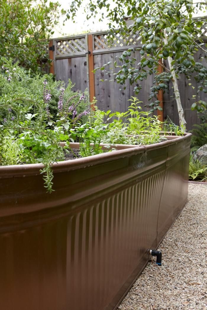 a large metal container filled with plants next to a wooden fence and shrubbery in the background