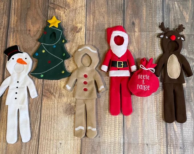 five christmas puppets are lined up on a wooden floor, one is wearing a santa suit and the other has a snowman