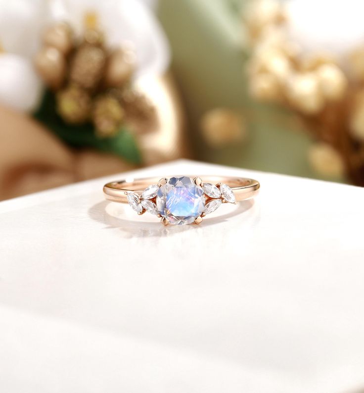 a ring with three stones sitting on top of a white table next to flowers and a vase