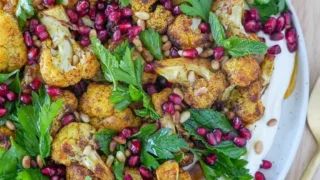 a white plate topped with cauliflower and pomegranate covered in greens