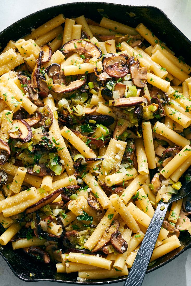 a skillet filled with pasta and mushrooms on top of a white tablecloth next to a knife