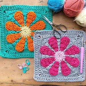 two crocheted squares with flowers on them and yarns next to each other