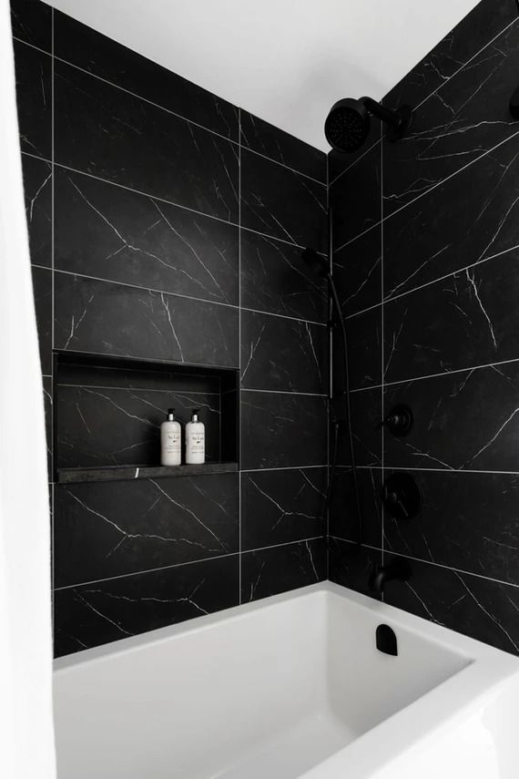 a black and white bathroom with marble tile on the walls, shower head, and bathtub