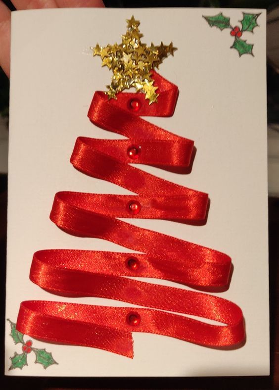 a hand holding a christmas card with red ribbon and gold stars on it, in front of a white background