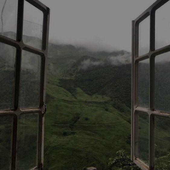 an open window looking out onto a green valley and mountains in the distance with fog