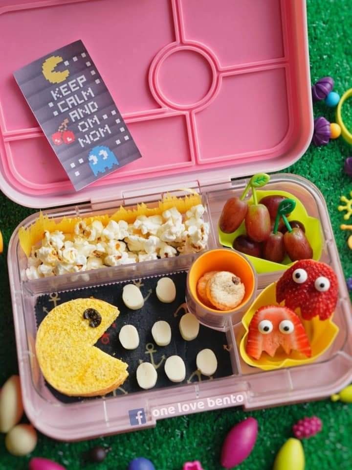 a pink lunch box filled with food on top of a green floor covered in eggs