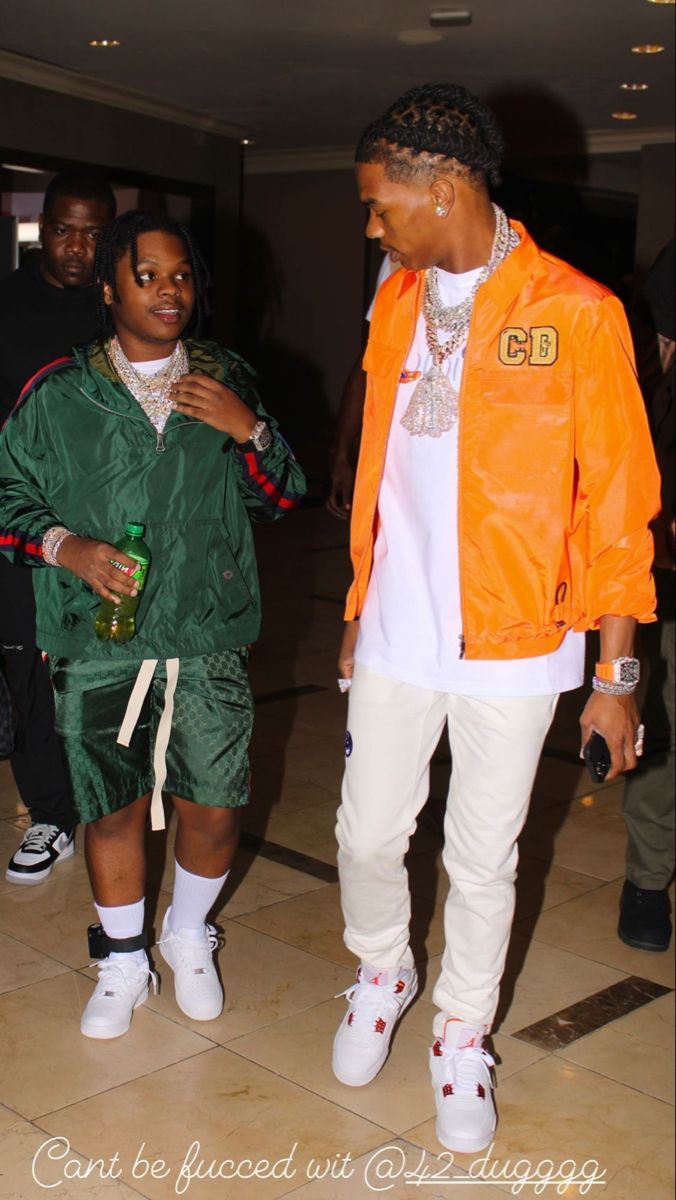 two people standing next to each other wearing orange jackets and white pants, one is holding a bottle