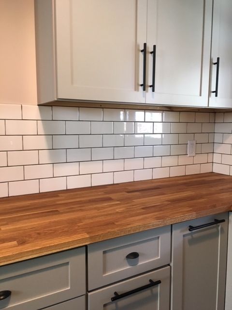 a wooden counter top in a kitchen with white cupboards and tile backsplash