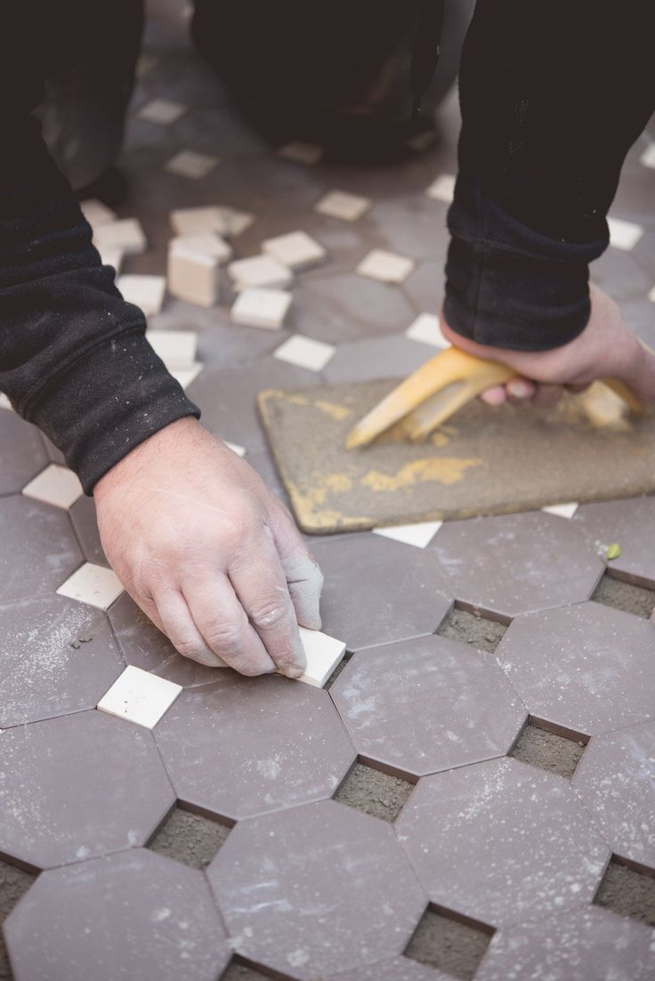 a person is working with cement on a tile floor that has been grouted