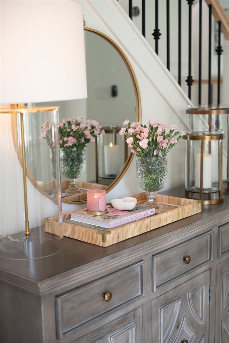 a table with flowers and candles on it in front of a mirror, lamp and stairs