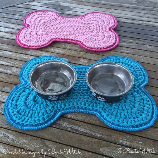 two dog bowls on top of a blue and pink mat with a bone shaped bowl in the middle