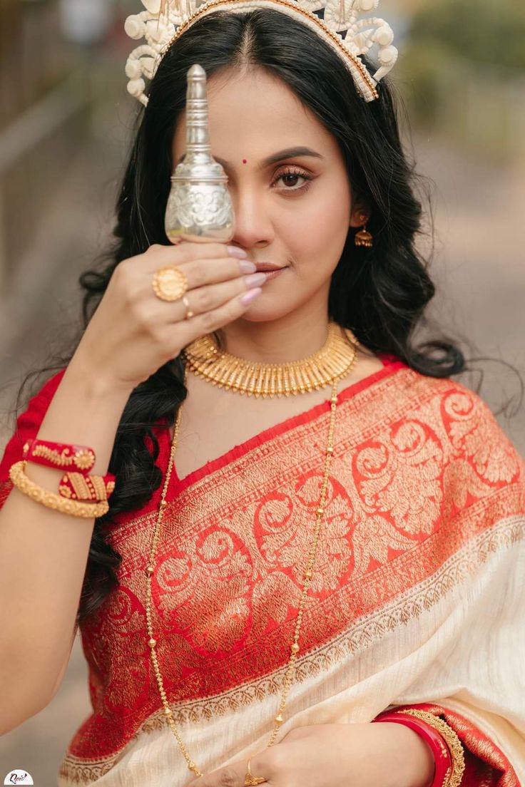 a woman in a red and white sari holding a silver object up to her face