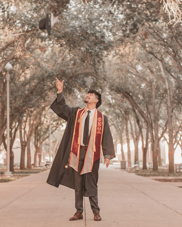 a graduate tossing his cap in the air while walking down a path lined with trees