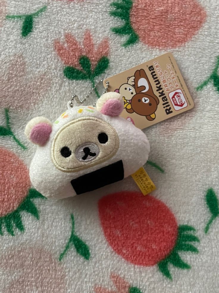 a small stuffed animal with a tag attached to it's ear sitting on a flowery blanket