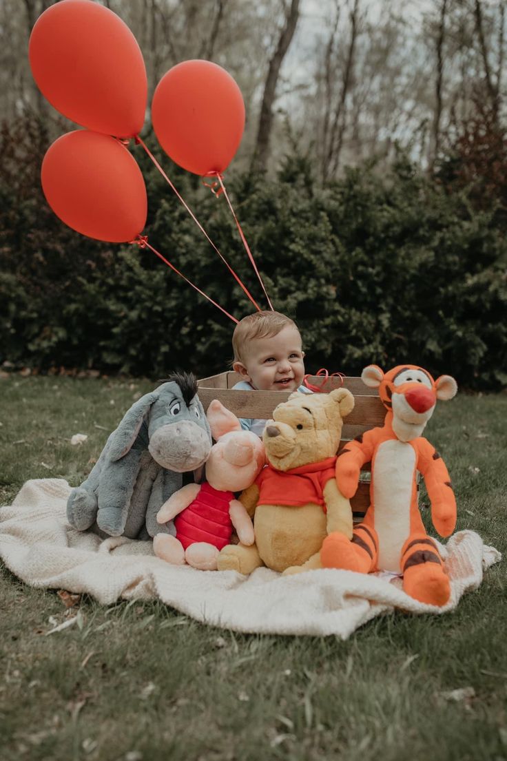 a baby sitting on a blanket with winnie the pooh and other stuffed animals