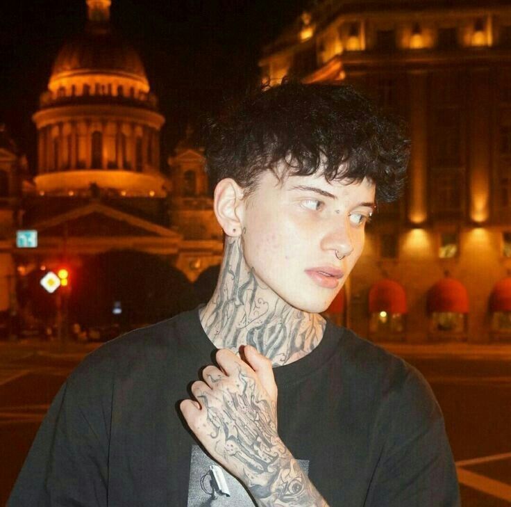 a young man with tattoos on his neck and arm standing in front of a building