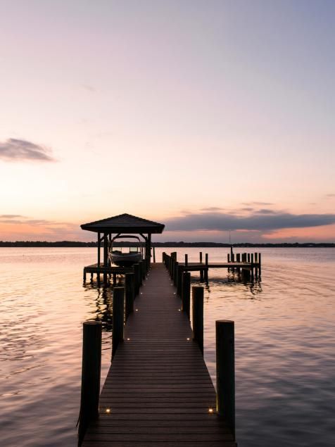 a dock that is sitting in the middle of some water at sunset with lights on it