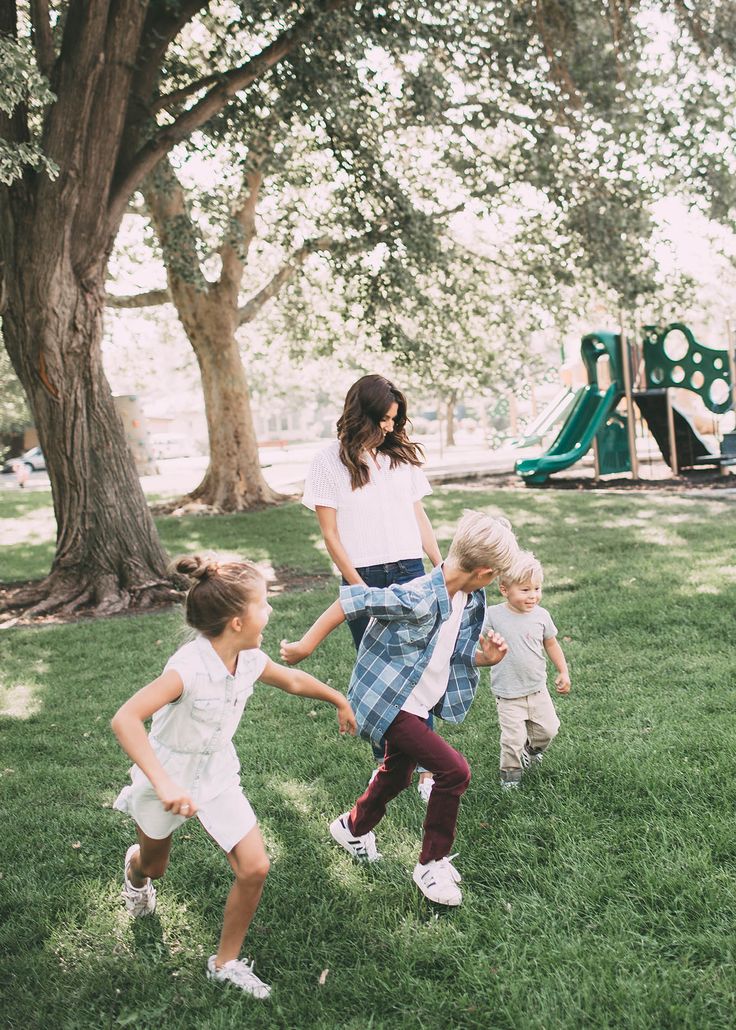 three young children playing in the grass near a tree