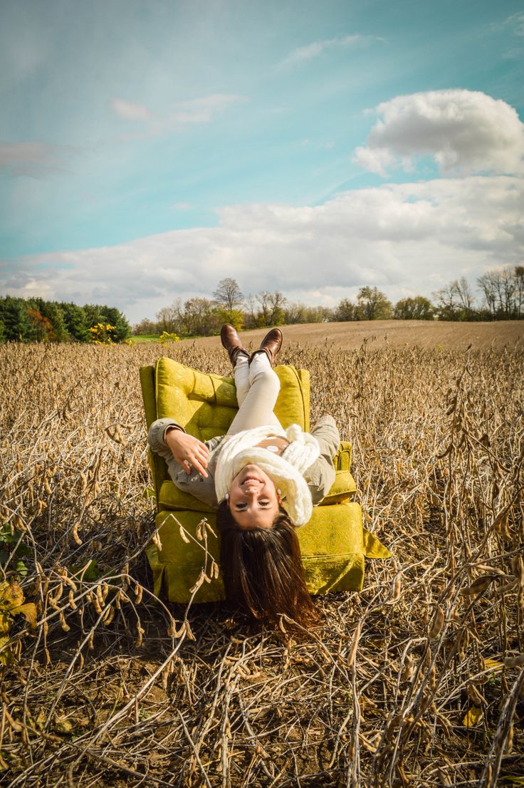 a woman laying on top of a yellow chair in the middle of a corn field