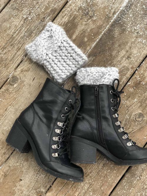 a pair of black boots sitting on top of a wooden floor next to a knitted boot