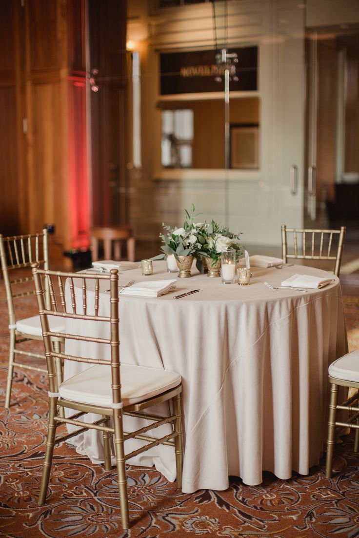 the table is set up with white linens and gold chairs for guests to sit at