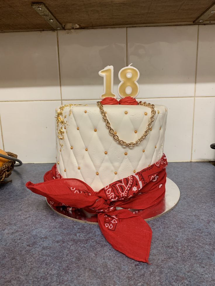 a white and red birthday cake with gold numbers on top, sitting on a blue countertop