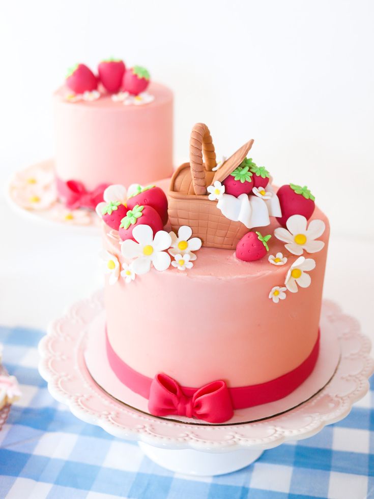 two cakes decorated with strawberries and flowers on a blue and white checkered tablecloth