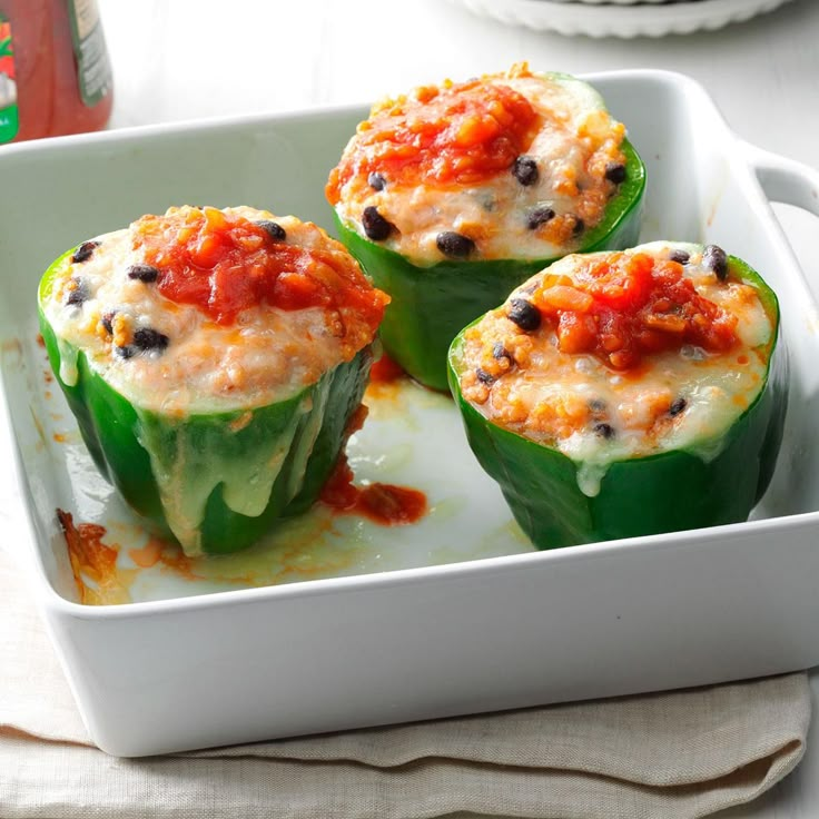 three stuffed peppers in a white casserole dish with sauce and cheese on top