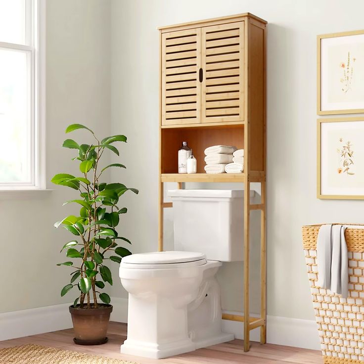 a white toilet sitting in a bathroom next to a wooden cabinet and potted plant