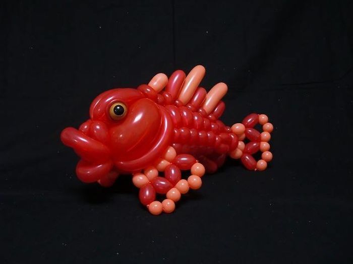 a red and orange balloon lizard sitting on top of a black surface with balloons attached to it's body