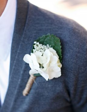 a boutonniere with white flowers and greenery on the lapel of a man