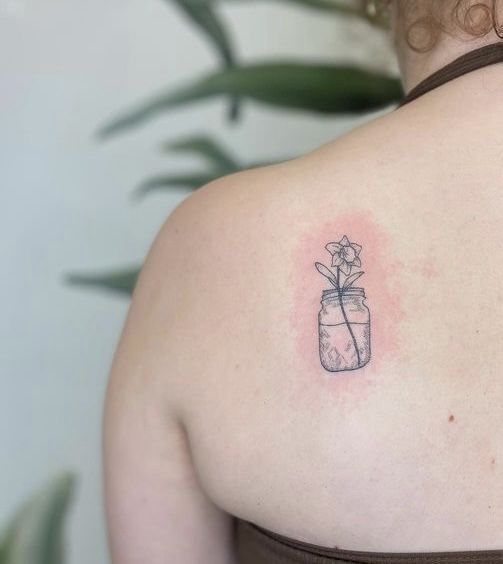 a woman with a flower in a jar tattoo on her upper back shoulder and arm