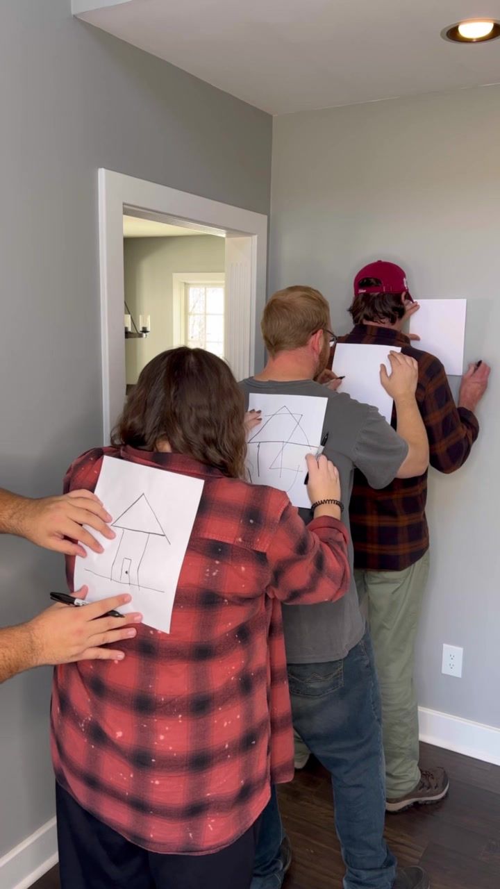 three people standing in a room with drawings on the wall and one person holding up a piece of paper