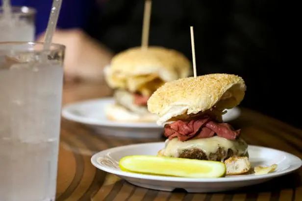 two white plates with sandwiches on them next to a glass of water and lemon wedges