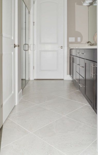 a white door is open in a large bathroom with gray cabinets and tile flooring