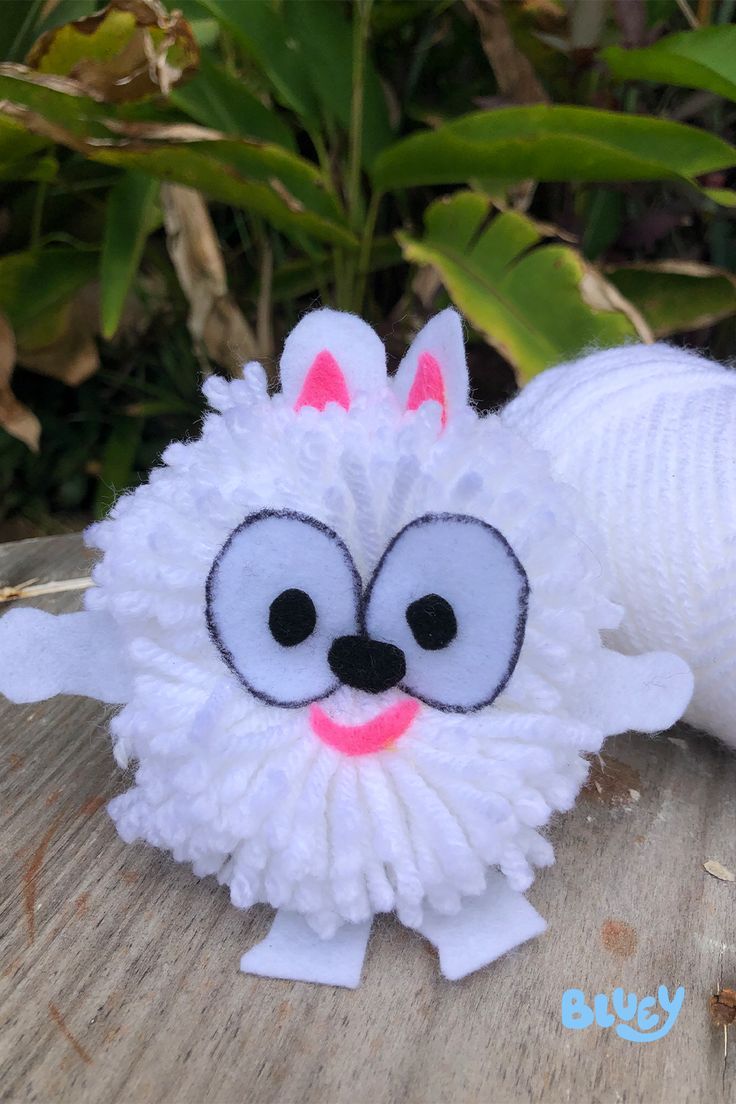 a white stuffed animal with big eyes and a pink nose sitting on a wooden surface