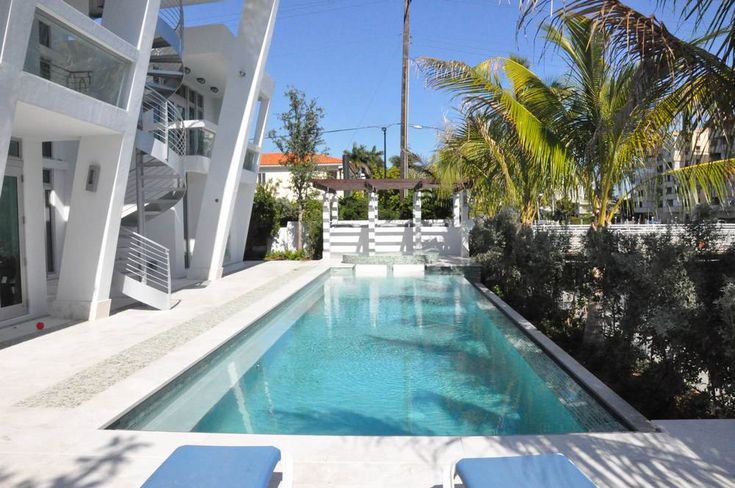 an outdoor swimming pool with lounge chairs next to it and palm trees in the background