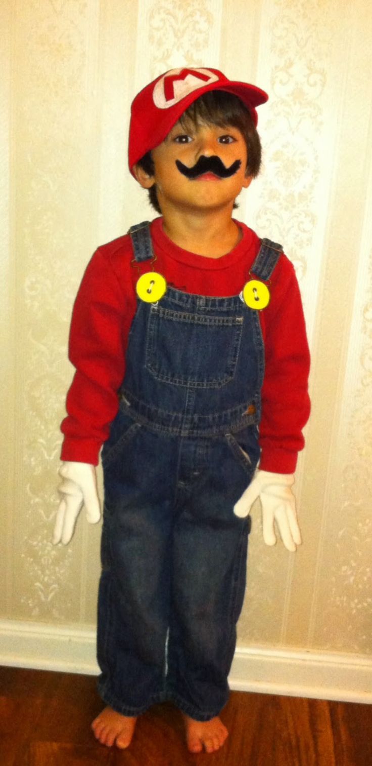 a young boy wearing overalls and a hat with fake moustache on his face