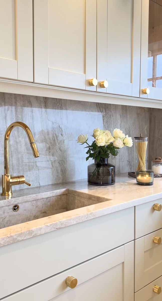 a white kitchen with marble counter tops and gold faucets on the sink area