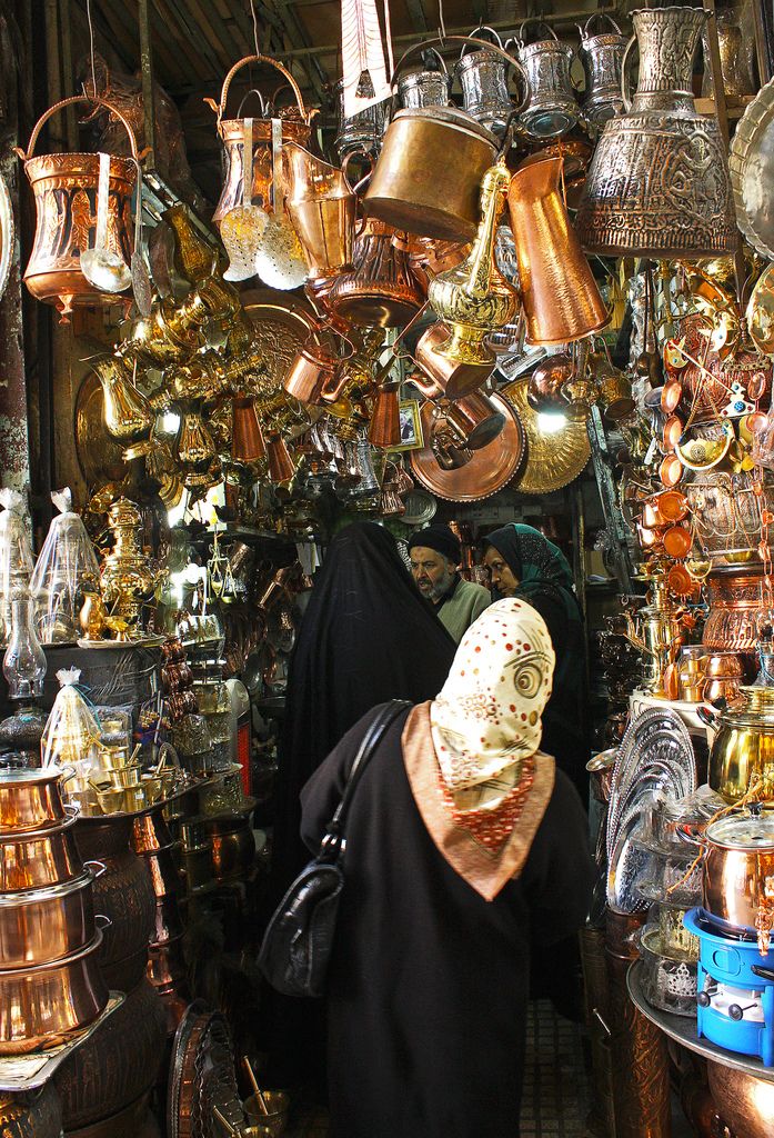 a woman wearing a black head covering in front of a store filled with copper pots and pans