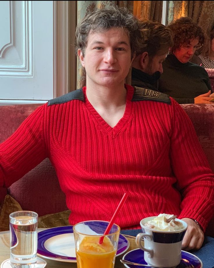 a man sitting at a table with two cups of coffee and orange juice in front of him