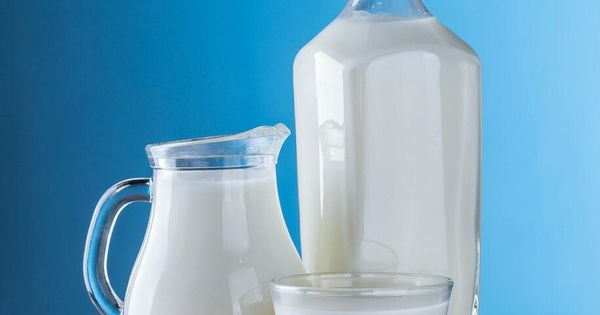 a bottle of milk next to two glasses and a jug on a table with blue background