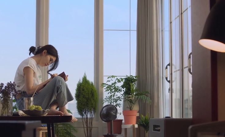 a woman sitting on the floor in front of a window looking at her cell phone